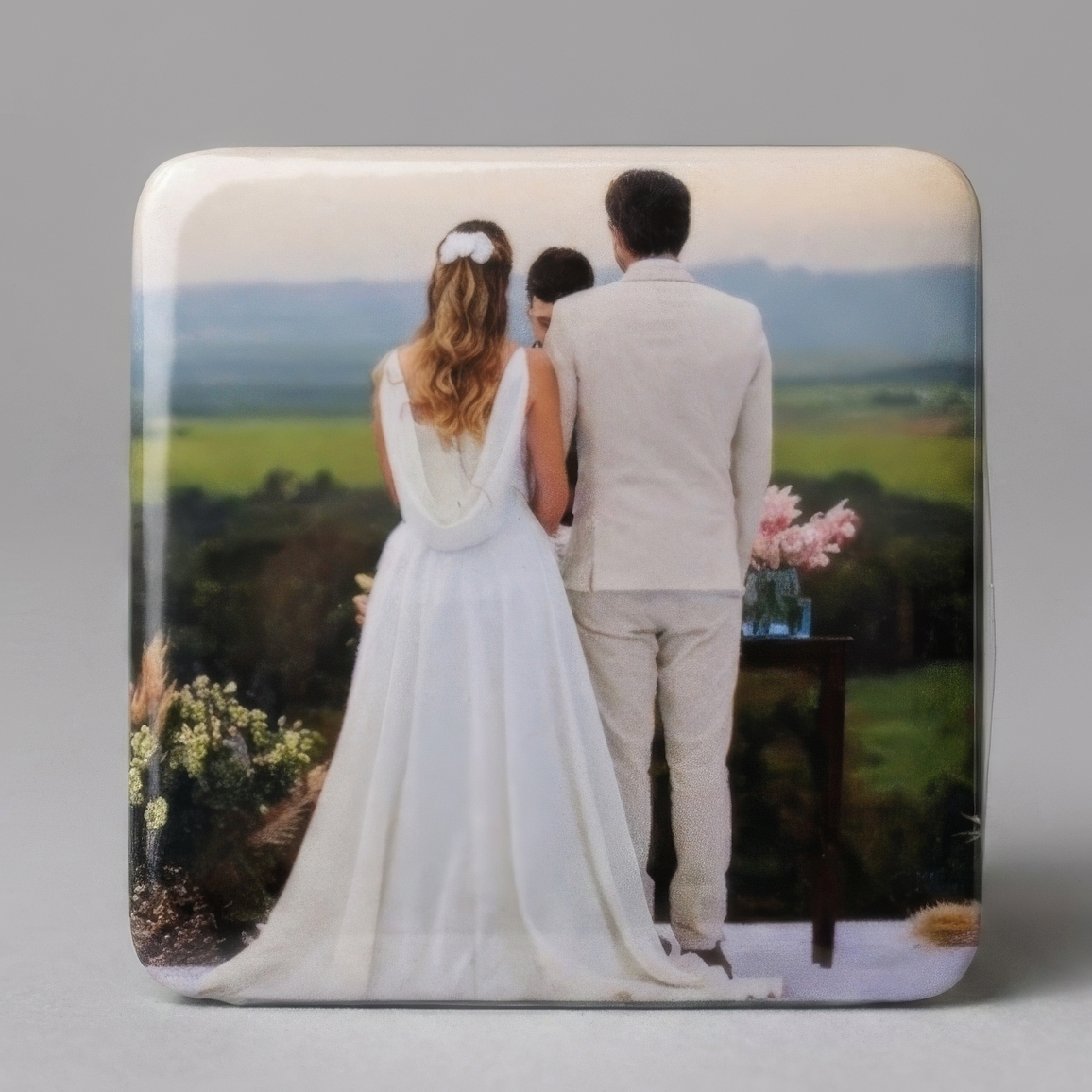 Ímã com foto de noivos de costas no altar ao ar livre, com campo verde ao fundo